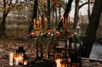 a mysterious enchanted forest fall wedding reception table done with orange candles, candle lanterns, greenery and bright blooms