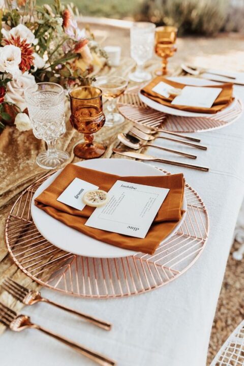 a pretty and cool boho micro wedding tablescape with copper placemats, rust-colored napkins, amber glasses and copper cutlery