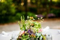 a pretty and small eclectic wedding centerpiece of moss, greenery and pastel and neutral blooms, candleholders and candle lanterns
