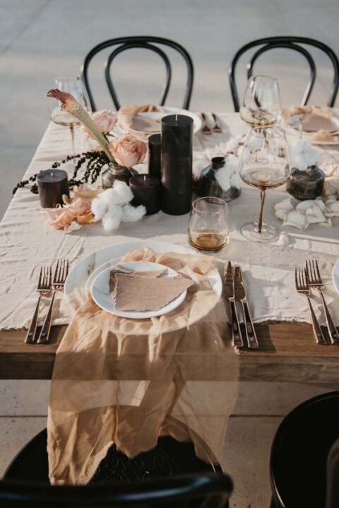 a refined modern micro wedding tablescape with neutral linens, raw edge cards, black candles, pink blooms and gold cutlery