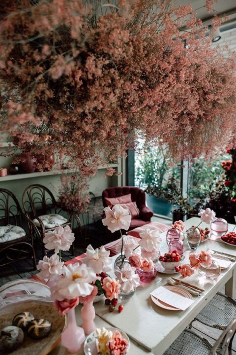 a romantic wedding reception table with blush blooms in pink vases, blush chargers, a cloud of pink blooms over the table