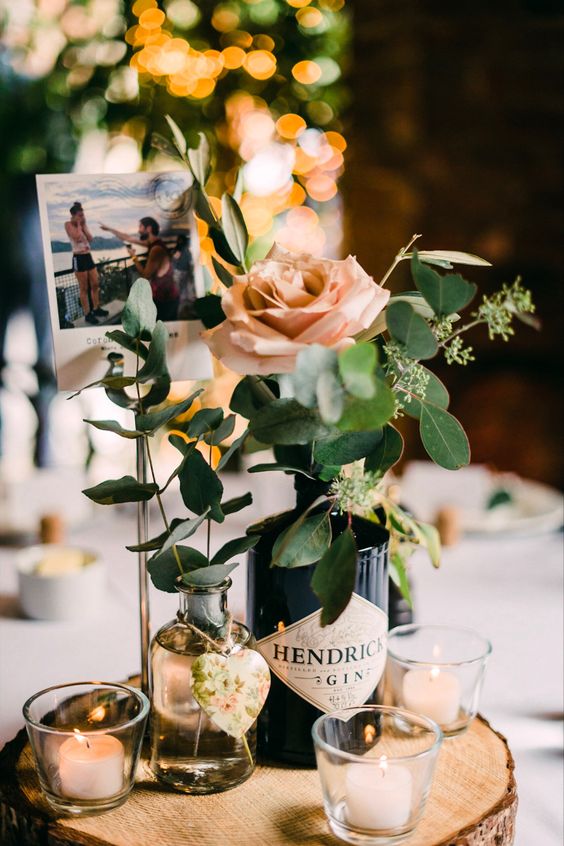 a simple eclectic wedding centerpiece of a tree slice, candles, a bottle with a rose and greenery, a bottle with a tag and a photo from the engagement