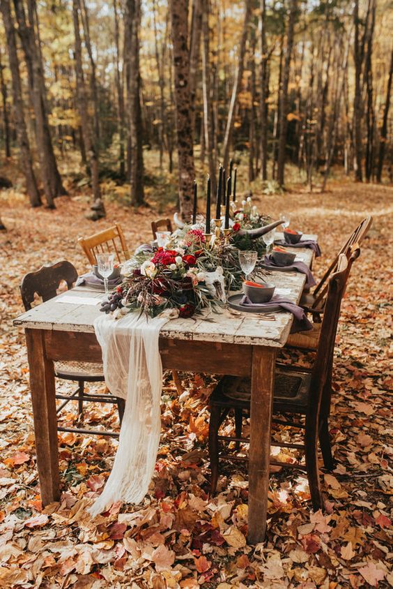 a small Gothic forest wedding reception with purple porcelain and napkins, with bold blooms and greenery, black candles and antlers