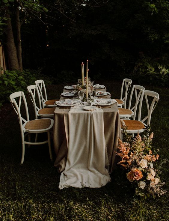 a small and cool outdoor wedding reception with neutral textiles, white porcelain and neutral candles and pastel blooms and greenery