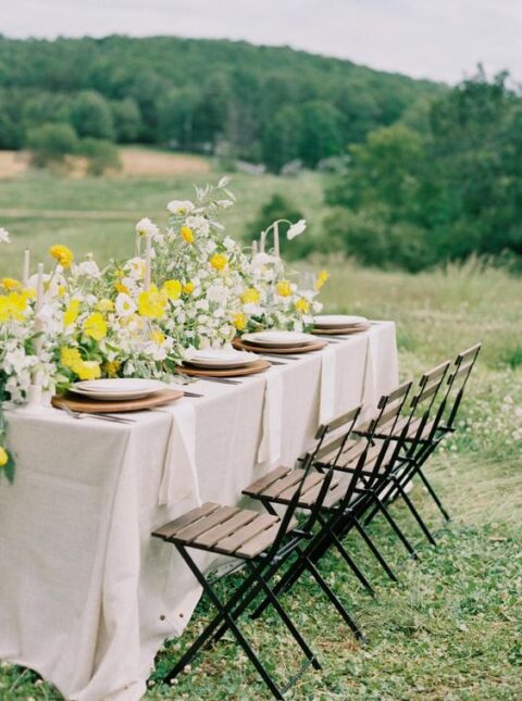 a sophisticated micro wedding reception table with neutral linens, white and yellow blooms, greenery and wooden chargers