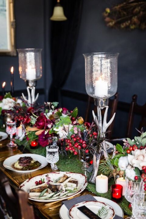 a super bold and refined fall enchanted forest wedding tablescape with a grass runner, dark foliage, bright berries, greenery, antler candleholders