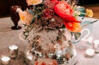 a super creative eclectic wedding centerpiece of a silver disco ball, bold blooms, greenery and dried flowers is amazing for a fun wedding