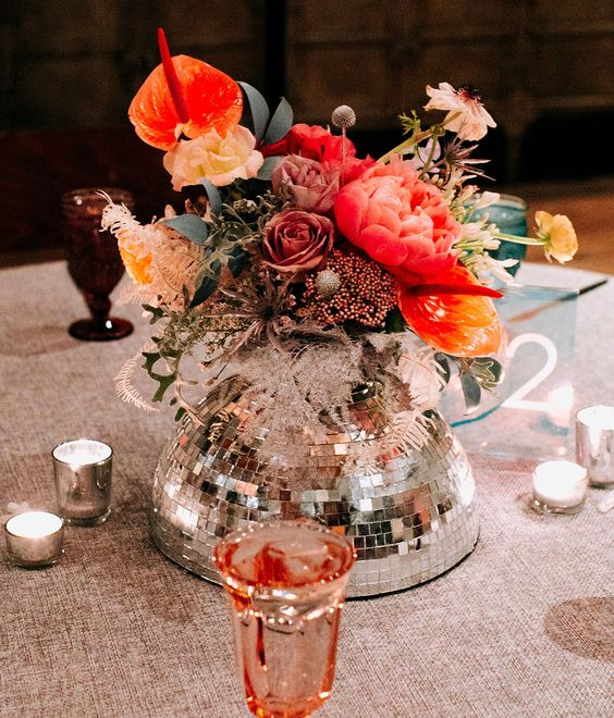 a super creative eclectic wedding centerpiece of a silver disco ball, bold blooms, greenery and dried flowers is amazing for a fun wedding