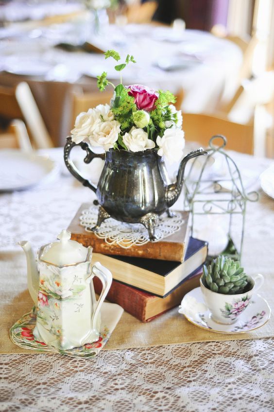 a vintage eclectic wedding centerpiece of a book stack, a succulent in a tea cup, a floral teapot and a metal coffee pot with blooms