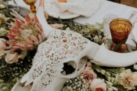 an eclectic boho wedding centerpiece of a carved animal skull, pink blooms and white ones, greenery is a bold statement