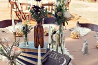 an eclectic boho wedding centerpiece of a doily, a book stack, bottles with bold blooms and greenery and a candle plus a table number