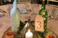 an eclectic wedding centerpiece of a tree slice with greenery, glitter pumpkins, a terrarium candleholder, a bottle with blooms and leaves and a bottle with lights