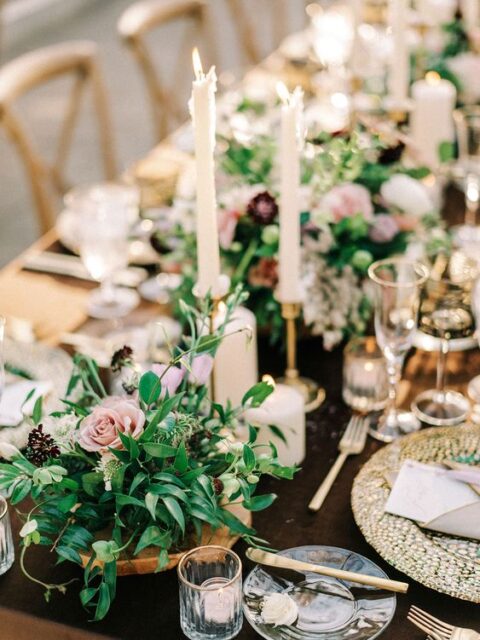an enchanted forest wedding table setting with greenery, pink blooms and berries and white candles, gold placemats and cutlery