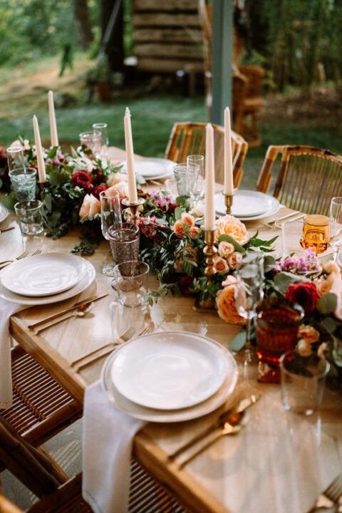 an exquisite micro wedding tablescape with a greenery and colorful bloom runner, candles, white plates, gold cutlery is amazing