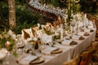 an extra long curved enchanted forest wedding table with tall candelabras covered with greenery and some blooms and wood slices as placemats