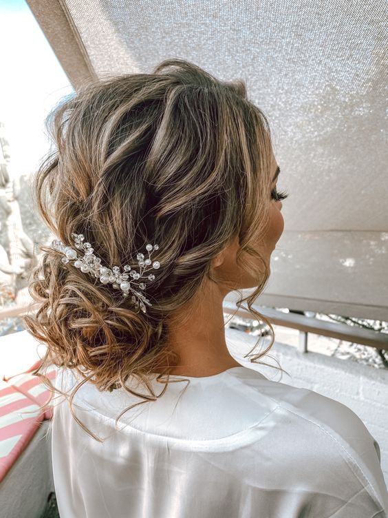 a messy wavy low bun with some locks down and a bead and pearl hair piece is a chic and cool idea for a wedding