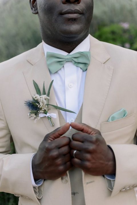 a tan suit, a white shirt and a sage green bow tie and handkerchief for a chic groom’s look