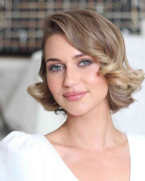 a chic light brown mid bob with blonde balayage and vintage curls on the ends is a sophisticated vintage wedding hairstyle