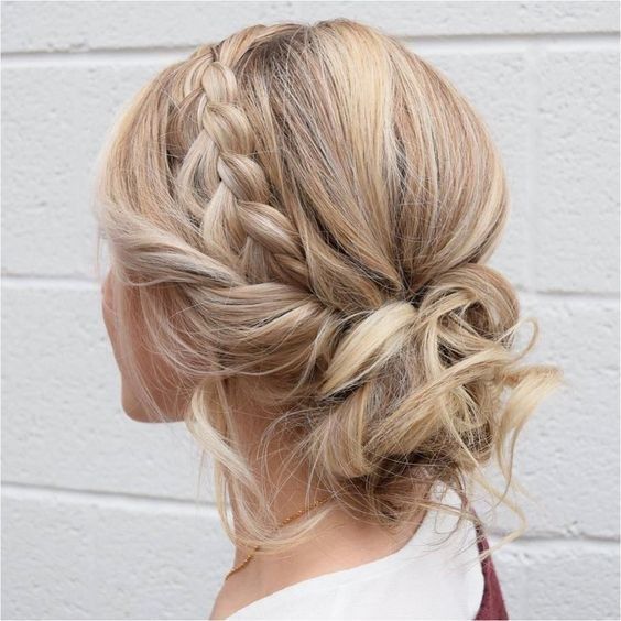 a cool messy and curly low updo with a braided halo and some locks and curls down for a boho or rustic bride