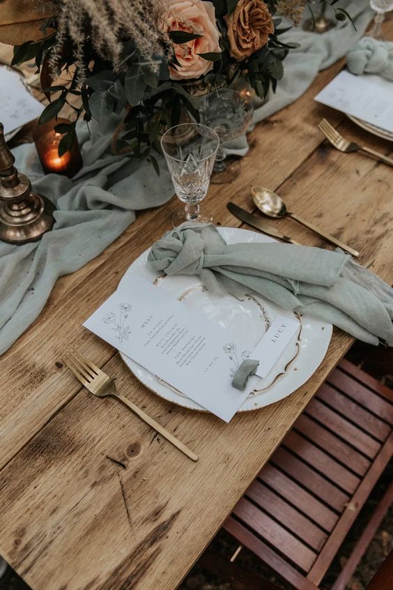 A boho wedding tablescape with sage textiles, neutral blooms, candles, gold rimmed glasses and gold cutlery