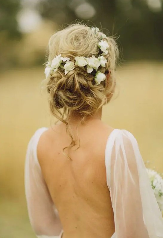 a messy and textured wavy low updo with some locks down and fresh blooms tucked in is a very chic and cool idea