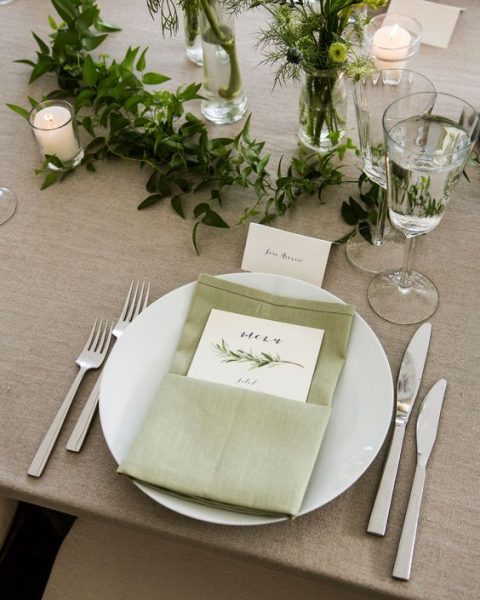 a chic wedding tablescape with a sage green napkin, a greenery runner and some candles