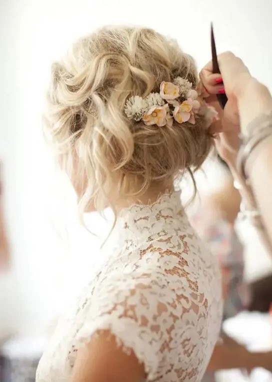 a messy and wavy wedding updo with small neutral flowers tucked in is a great idea for a spring boho bride