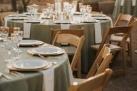 21 a cozy wedding reception space with sage green tablecloths and neutral napkins, gold-rimmed glasses and gold cutlery