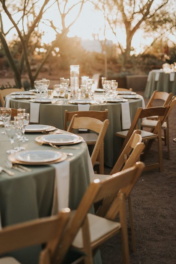 A cozy wedding reception space with sage green tablecloths and neutral napkins, gold rimmed glasses and gold cutlery