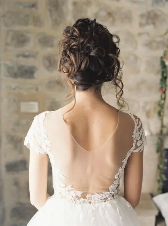 a messy curly wedding updo is a natural and chic choice and some locks down will create a movement effect instantly