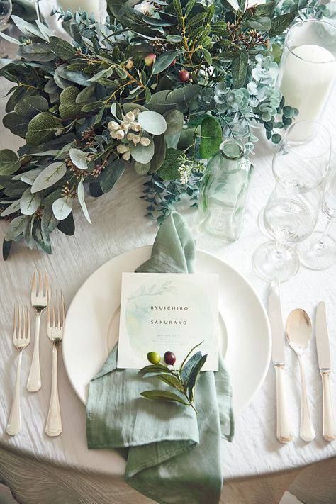 a gorgeous wedding tablescape with greenery and blooms, neutral porcelain, a sage green napkin, some chic cutlery and candles