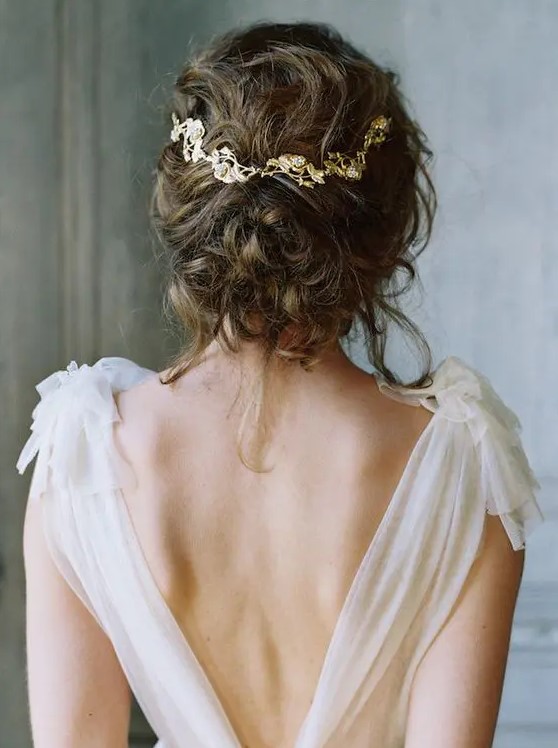 a messy curly wedding updo with a gold and rhinestone hair vine is a lovely idea for an effortlessly chic bride