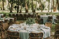 26 a lovely outdoor wedding tablescape with a sage green tablecloth and neutral napkins, greenery and amber glasses, rattan chairs