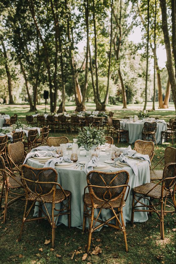 a lovely outdoor wedding tablescape with a sage green tablecloth and neutral napkins, greenery and amber glasses, rattan chairs
