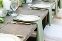 27 a lovely rustic wedding tablescape with an uncovered table, sage green napkins and greenery, pilalr candles and gold cutlery