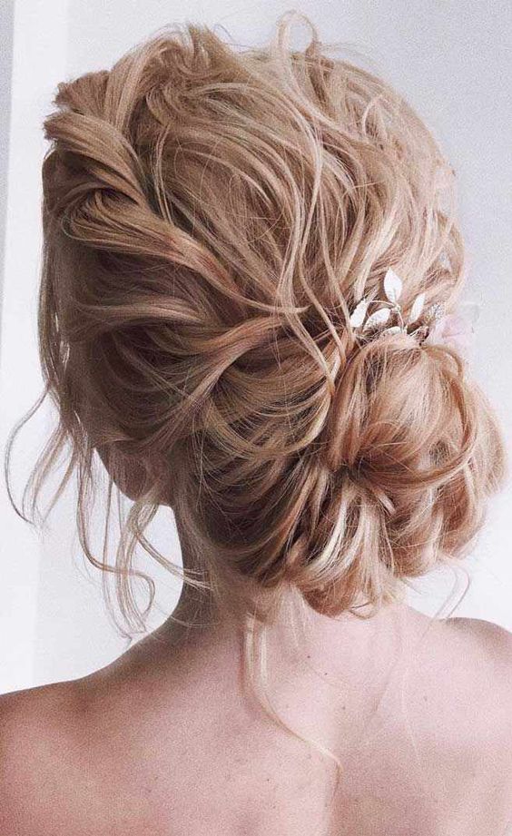 a messy wavy low bun with a wavy top, a braided touch, a low bun and a leaf hair piece is amazing