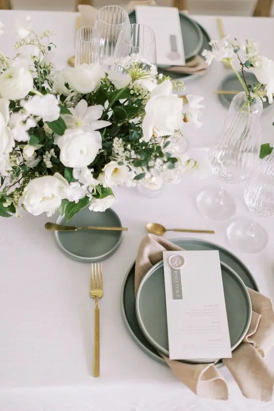 a luxurious sage green, white and gold wedding tablescape with a neutral floral centerpiece, sage green plates and gold cutlery