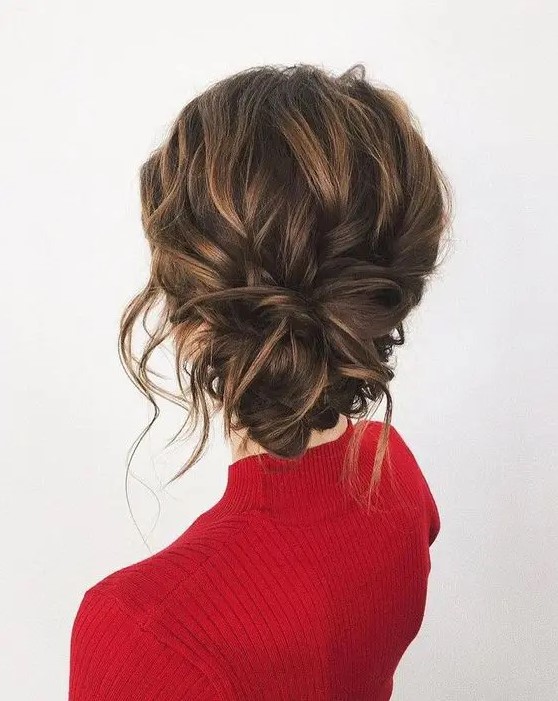 a messy wavy updo with a low twsited bun, some locks down and a volume on top