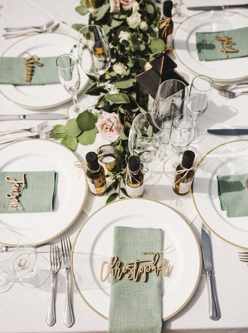 a neutral wedding table setting with neutral porcelain, sage green napkins, greenery and blush blooms and calligraphy cards