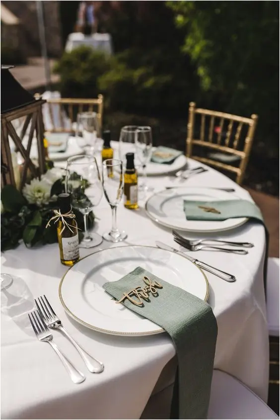 a rustic wedding tablescape with a wooden lantern and neutral blooms, white porcelain, sage green napkins is a lovely one