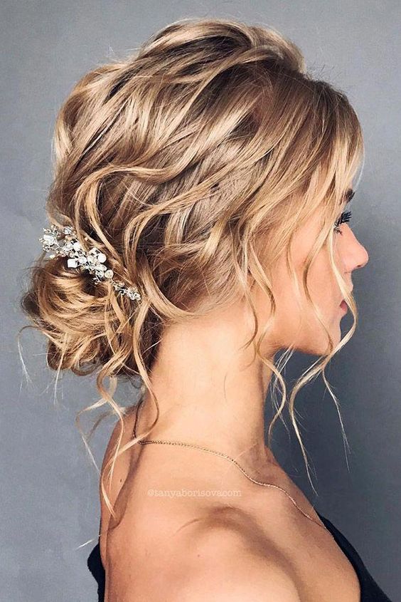 a wavy low bun with a wavy top and some locks down, a rhinestone and pearl hair piece is a chic and cool idea