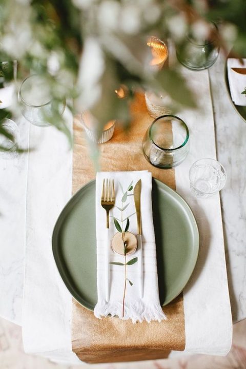 a stylish wedding tablescape with a sage green charger, green glasses and gold touches for elegance