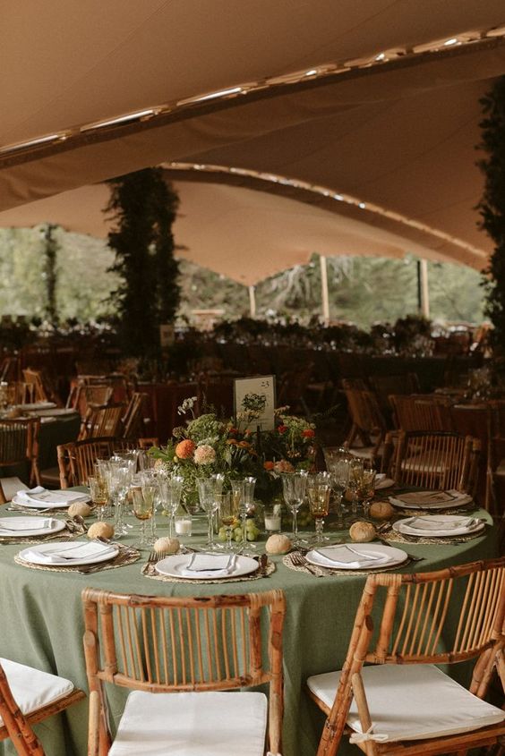 a welcoming fairy-tale wedding tablescape with a sage green tablecloth, bold blooms and greenery and gold-rimmed glasses