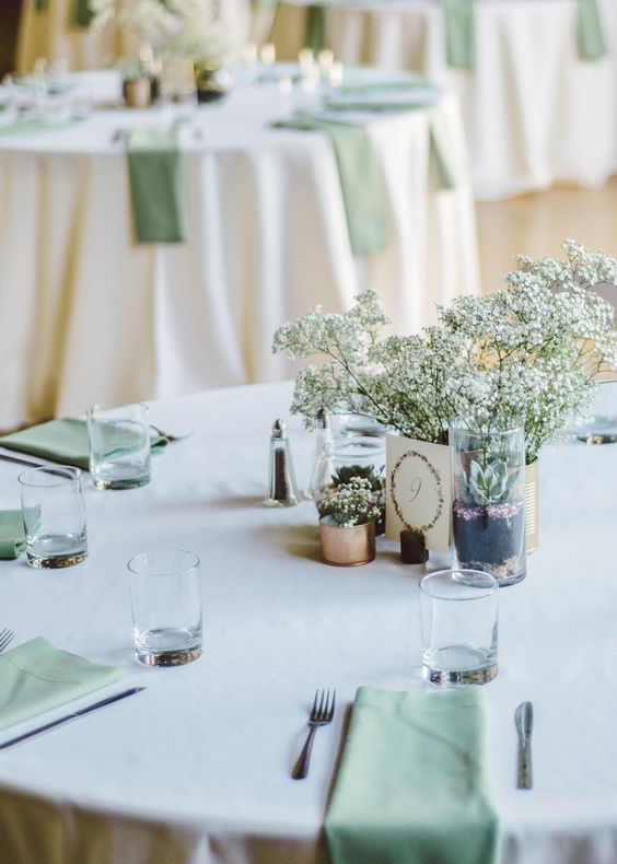 an airy wedding tablescape with a white tablecloth, sage green napkins, baby's breath and succulents is modern and simple