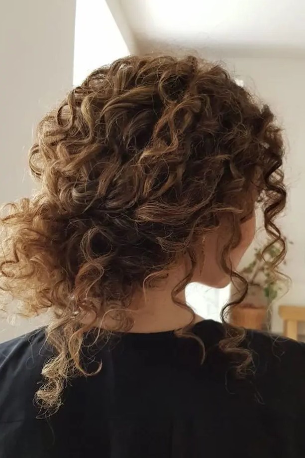A curly messy low bun with bangs is a timeless idea for girls with curls   looks very pretty and relaxed