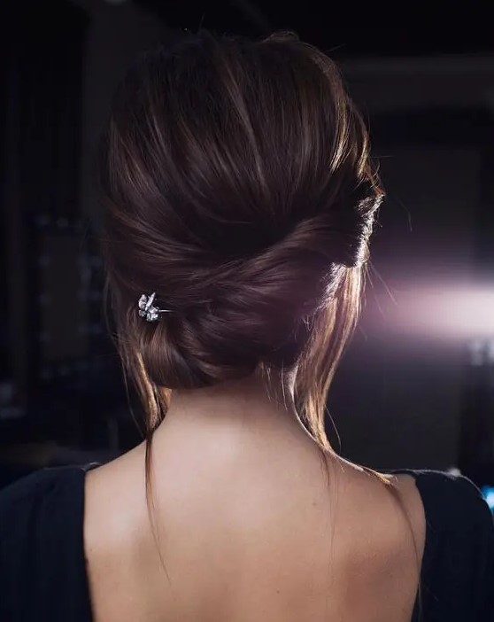 a chic twisted low chignon with some bangs down and a little rhinestone hairpiece for a modern bride