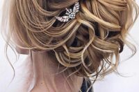 47 a sophisticated wavy wedding updo with a lot of hair, a volume on top and some locks down plus a rhinestone hairpiece