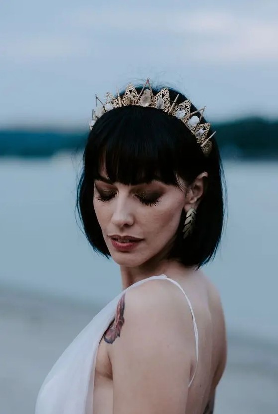 a stylish black bob with fringe and a gold and crystal crown plus matching gold earrings for a bold modern bridal look