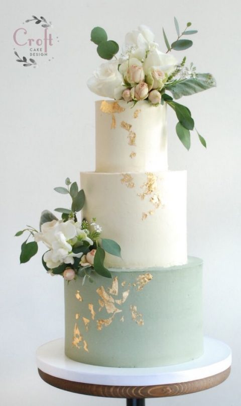 a chic wedding cake with white and sage green tiers and fresh blush and white blooms plus gold leaf