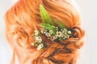 a gorgeous ginger twisted low updo with some locks down and some fresh blooms and greenery is a cool idea for a boho bride